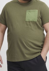 Olivengrøn kortærmet t-shirt lavet af bomuld med en struktureret lomme i en lysere grøn farve. Regular fit med en lige søm.