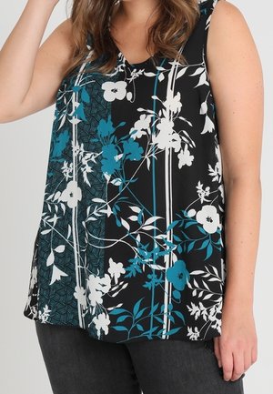 Czarna bluzka bez rękawów z białymi i turkusowymi kwiatowymi i liściastymi wzorami, noszona z ciemnymi spodniami.