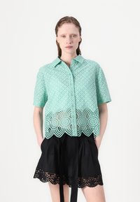 Mintgroene shirt met korte mouwen met een gaatjesontwerp en een schulp kantzoom, gecombineerd met zwarte shorts met kantafwerking en een strik in de taille.