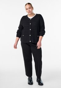 Svart stickad cardigan med en strukturmönster, knappstängning fram och två fickor. Matchad med svarta byxor och ankelstövlar.