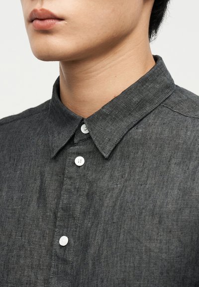 Κοντινή λήψη ενός ατόμου που φοράει σκούρο γκρι πουκάμισο με κουμπιά και μυτερό γιακά, εμφανίζοντας το κάτω μέρος του προσώπου και τον λαιμό.