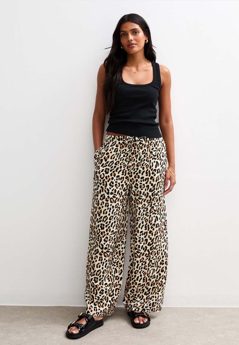 Leopardenmuster weite Hosen mit elastischem Bund, kombiniert mit einem schwarzen gerippten Tanktop und schwarzen Rutschsandalen. Glattes Material, lässiges Design.