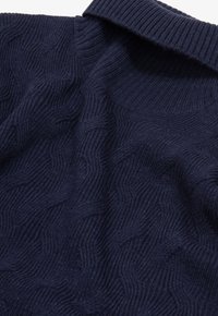 Marineblauer Strickpullover mit Wellenmuster, geripptem Kragen und weicher Textur. Der Stoff wirkt dick und kuschelig.