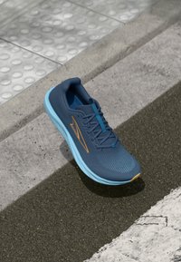 Baskets de course bleues avec une tige en maille texturée, des accents oranges et une semelle intermédiaire bleu clair. Comprend un col rembourré et des lacets plats.