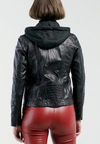 Schwarze Lederjacke mit taillierter Passform, ausgestattet mit einer abnehmbaren schwarzen Kapuze. Glatte Textur mit Nahtdetails und enganliegenden roten Hosen.