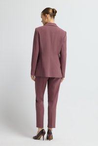 Costume mauve comprenant un blazer ajusté et un pantalon slim, confectionné dans un tissu lisse ; associé à des chaussures à talons hauts bordeaux.