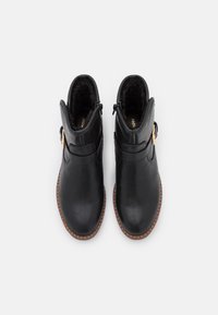 Botas de cuero negro hasta el tobillo con un suave forro interior, punta redonda y cremalleras laterales. Presentan un detalle de hebilla decorativa y suela marrón.