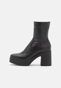 Stivale alla caviglia in pelle nera con suola a pianta alta e tacco a blocco. Presenta una texture liscia e un design elegante e aderente.