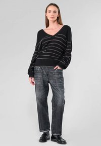 Zwarte oversized trui met zilveren horizontale strepen, V-hals ontwerp, gecombineerd met donkergrijze, losse jeans met zijzakken.