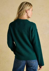 Pulover din lână verde închis, cu un guler cu nervuri și un finisaj texturat, având umeri lăsați și o croială lejeră, văzut din spate.