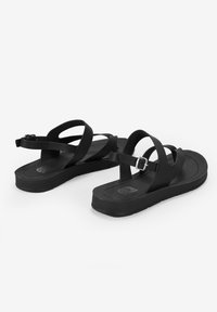 Sandali neri con design a strisce, materiale in gomma, suola piatta, cinturino alla caviglia regolabile e branding minimalista sulla soletta.