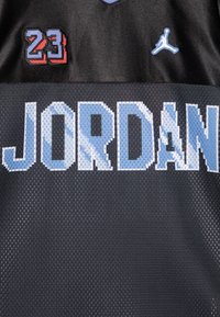Canotta da basket nera con "JORDAN" in grandi lettere pixelate blu, il numero ricamato "23" in rosso e blu, e un logo Jumpman blu.
