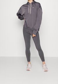 Gray hoodie with pink drawstrings and matching leggings in stretch fabric. Sneakers feature a light color with subtle accents.