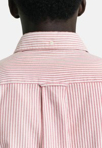 Randig skjorta med röda och vita vertikala ränder, med en knapp-ned krage och en ok baktill. Texturerad tyg för extra detalj.