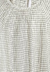 Kevyt, teksturoitu kangas ruutukuviolla off-white ja mustana, jossa on kerrostettua yksityiskohtaa kaula-aukossa ja hartioilla.