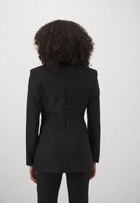 Black tailored blazer featuring structured shoulders, a fitted silhouette, and smooth fabric; displayed from the back with a clean design.