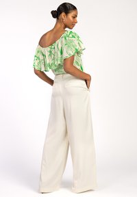 Off-the-shoulder top in het wit met een groen bloemenpatroon, gecombineerd met hoge taille, wijde broek in crèmekleur met zijzakken.