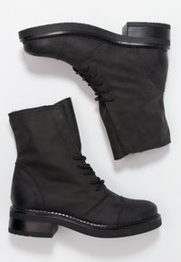 Bottes chelsea en cuir noir avec un bout arrondi, un laçage à l'avant, un petit talon carré et des détails cousus le long de la semelle. Tige texturée.