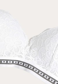 Biała koronkowa braletka z kwiatowym wzorem, falbaniastymi krawędziami i szerokim białym pasem z czarnymi akcentami oraz tekstem logo.