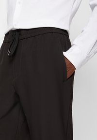 Svarta byxor med elastisk midja och sidofickor, som har en avslappnad passform och en mjuk yta, kombinerade med en vit skjorta med knappar.