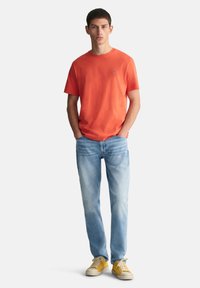 Kortermet oransje T-skjorte, lyseblå jeans og gule joggesko. Avslappet passform med rund hals og minimal detaljering.