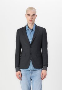 Temno siv eleganten blazer s dvema gumboma, z nazobčanimi reverji in sprednjima žepoma, nosi se čez svetlo modro denim srajco. Gladka tekstura.