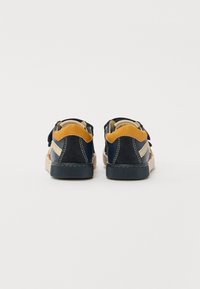 Pantofi din suede navy cu accente bej și panouri bej. Dispune de o talpă plată din cauciuc și două benzi Velcro pentru o îmbrăcare ușoară.