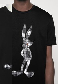 Black T-shirt featuring a houndstooth-patterned cartoon rabbit graphic on the front. Round neckline and short sleeves.
