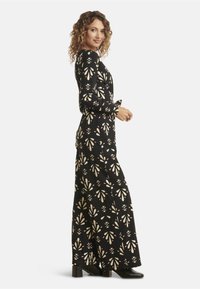 Long black dress with cream floral pattern, long sleeves, and fitted bodice, flowing skirt, paired with black heeled boots.