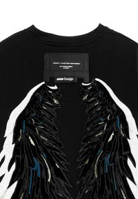 Camiseta de algodón negra con grandes diseños de alas en bordado negro, blanco y azul, con una etiqueta en el cuello que muestra la información de la marca.