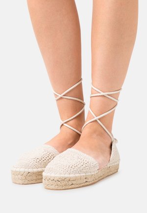 Beige gehaakte espadrilles met een geweven jute zool en gekruiste stoffen banden rond de enkel, met een gestructureerde bovenkant en een puntige neus. 
