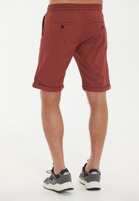 Burgundy shorts med uppvikta kanter, elastisk midja, två bakfickor med knappstängning och en slät bomullstextur.