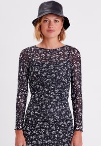 T-shirt noir à manches longues avec imprimé floral, pr�ésentant des détails froncés et un col rond, associé à un chapeau seau noir.