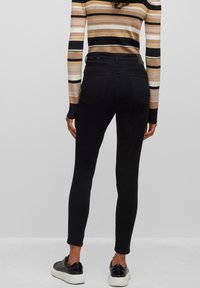 Jeans negros ajustados con cintura alta, que cuentan con dos bolsillos traseros y una textura suave. Combinados con zapatillas negras y una camiseta de rayas multicolores.