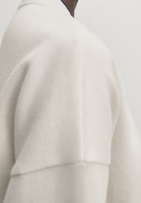 Cream-colored oversized sweater with textured fabric, dropped shoulder seams, and a clean, minimal design.