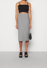 Svart kort topp och högmidjad houndstooth midi kjol. Genomskinlig textur med ett subtilt mönster. Bärs med plattformsskor i svart och en liten väska.