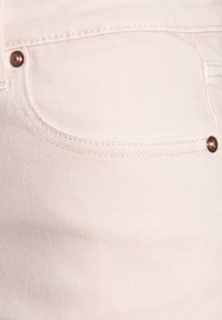 Gaiši rozā denim audums ar teksturētu apdari, ar mazu kabatu un varškrāsas pogu akcentiem. Ir redzama smalki diagonāla ribbinga struktūra.