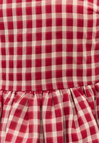 Tissu vichy rouge et blanc avec un détail froncé créant un effet volanté le long de la ligne de couture.