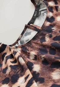 Blouse à imprimé léopard marron et noir avec col rond et détail froncé près de l'épaule, étiquette « NEXT » à l'intérieur du col.