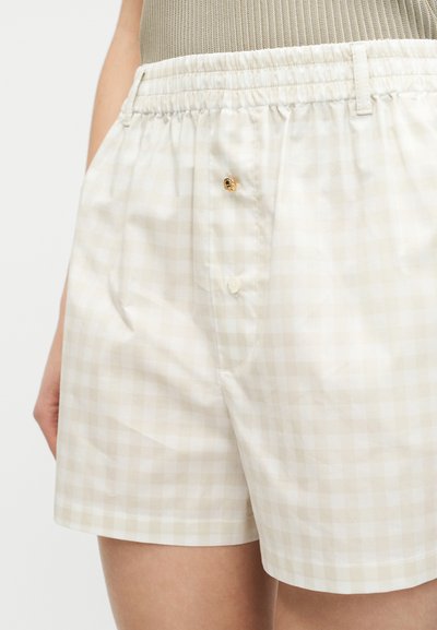 Μπεζ και λευκά καρό σορτς με ελαστική μέση και λεπτομέρειες με κουμπιά, φορεμένα με μπεζ ριμπ τοπ που είναι μαζεμένο μέσα.