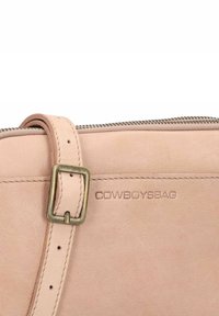 Borsa a tracolla in pelle rosa chiaro con chiusura a zip, dettaglio in ottone e logo del marchio impresso. Texture liscia con dettagli di cucitura.