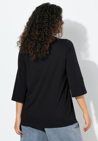 Czarna bluzka z rękawami do łokcia o luźnym kroju, z zaokrąglonym dekoltem i miękką fakturą, zestawiona z jasnoniebieskimi dżinsami.