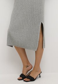 Graues geripptes Strickkleid mit Seitenschlitzen, kombiniert mit schwarzen geflochtenen Absatzsandalen. Glatte Textur, mittellanges Design und taillierte Silhouette.