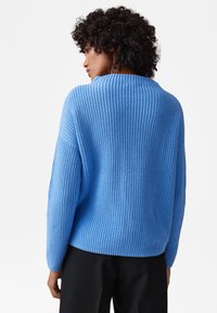 Maglione lavorato a maglia di colore azzurro chiaro con una vestibilità rilassata, caratterizzato da una texture a coste e un collo rotondo, abbinato a dei pantaloni scuri.