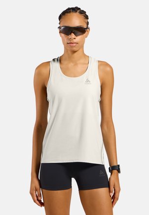 Femme portant un débardeur de sport gris clair, un short noir, des lunettes de soleil de sport noires et une montre-bracelet noire sur un fond uni.