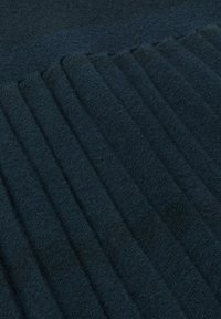 Tumman teal värinen neulottu kangas, jossa on ribbikuvio ja pystytaskut antamassa syvyyttä ja visuaalista mielenkiintoa. Pehmeä ja sileä pinta.