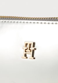 Metalni srebrni etui z zlatim zadrgo. Na sprednji strani se nahaja izstopajoč zlat logotip 'TH'. Gladka tekstura, minimalističen dizajn.