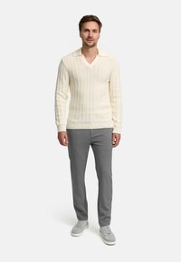 Maglione a costine crema con scollo a V e collo, abbinato a pantaloni grigi a gamba dritta e sneakers grigio chiaro. Design semplice, tessuto Texturizzato.