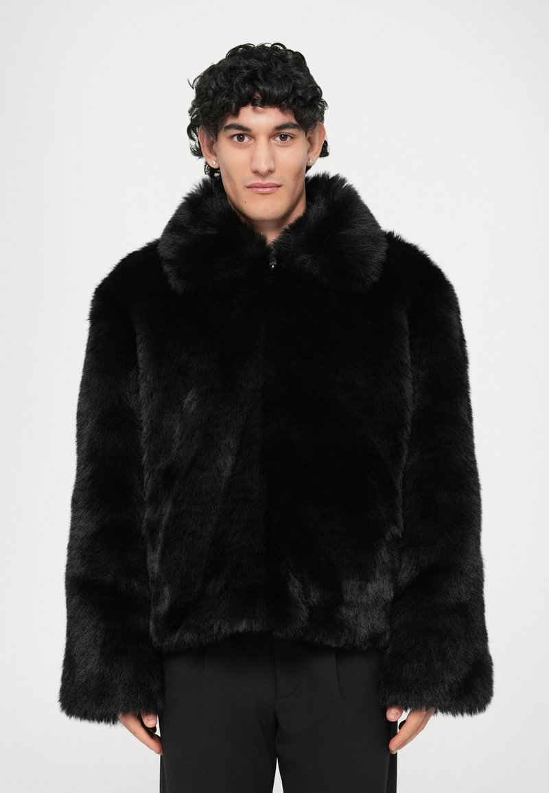 Zwarte nepbont jas met een brede kraag, lange mouwen en een cropped ontwerp. De stof lijkt zacht met een gladde textuur.