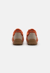 Orange and beige footwear with mesh and suede materials, featuring a padded collar and textured rubber sole. Logo is visible on heel.